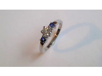 Three stone ring set with one round brilliant cut diamond and two blue sapphires, all in claw settings.