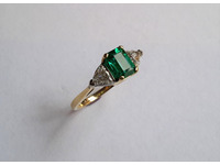 18ct yellow gold ring set with centre octagonal emerald and one trillion diamond on each shoulder.